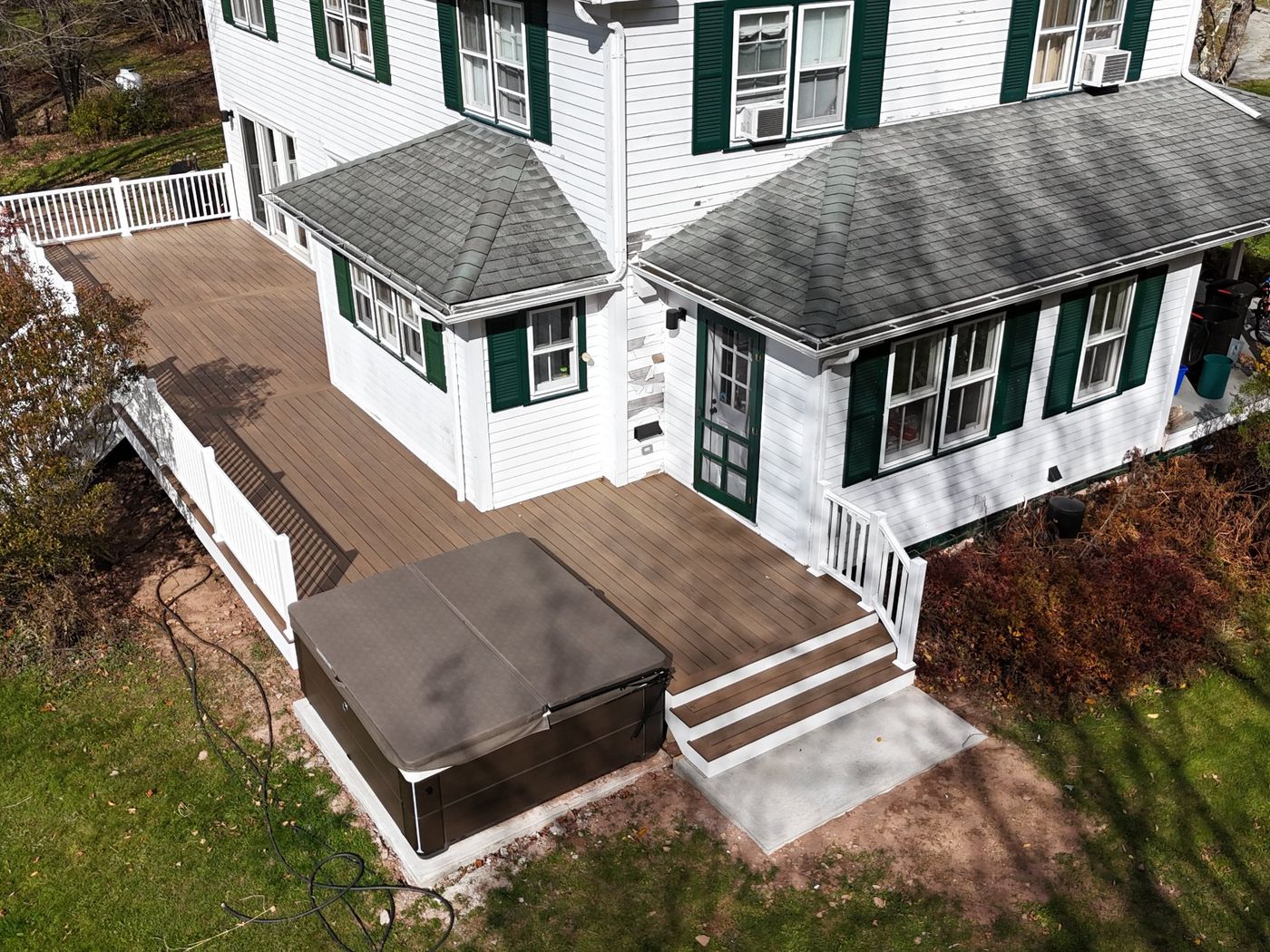 The finished composite deck with white railings, steps and the hot tub on its pad
